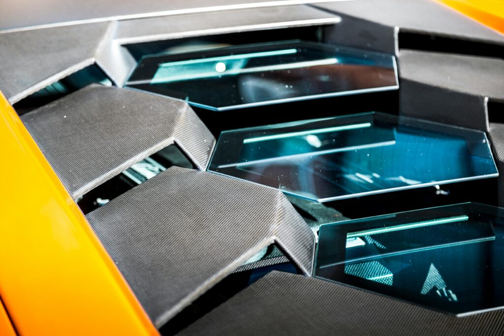 Detailed close-up of a luxury sports car's sleek and artistic design elements under bright sunlight.